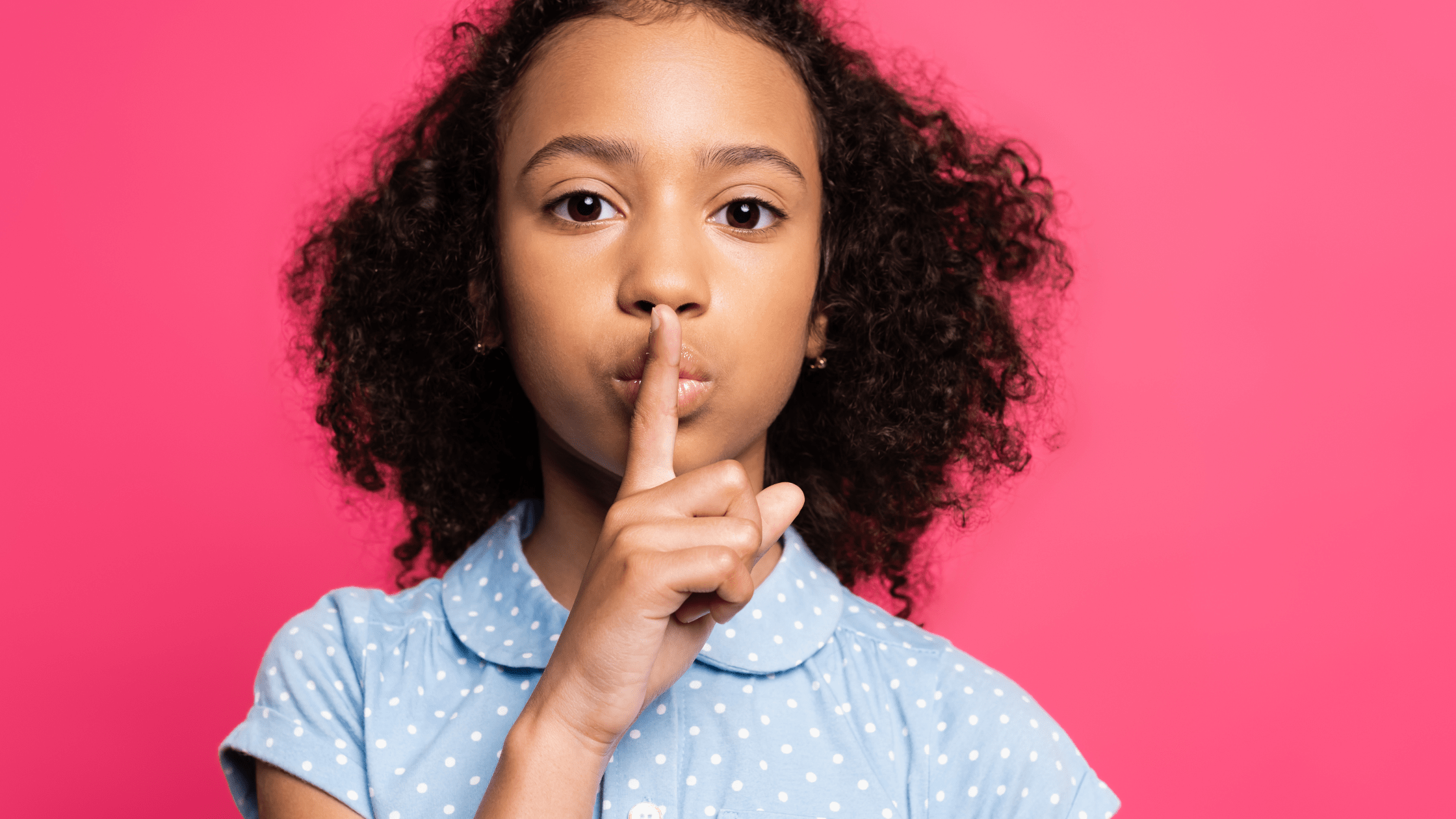 Little girl saying be quiet by placing finger on her lips